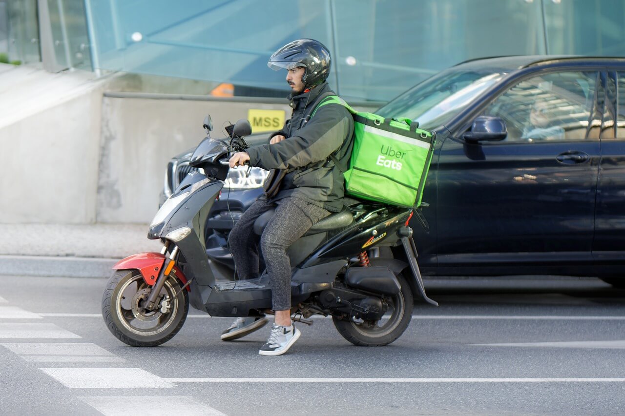 A delivery driver on a scooter bringing a food order to a customer.