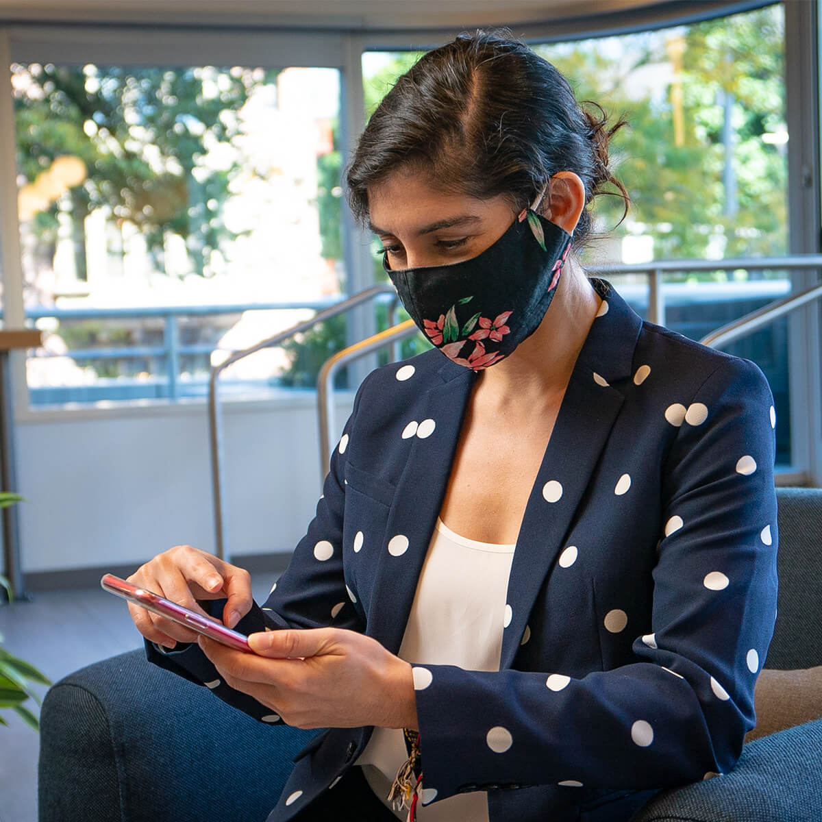 A formally dressed woman wearing a face mask checking her phone.