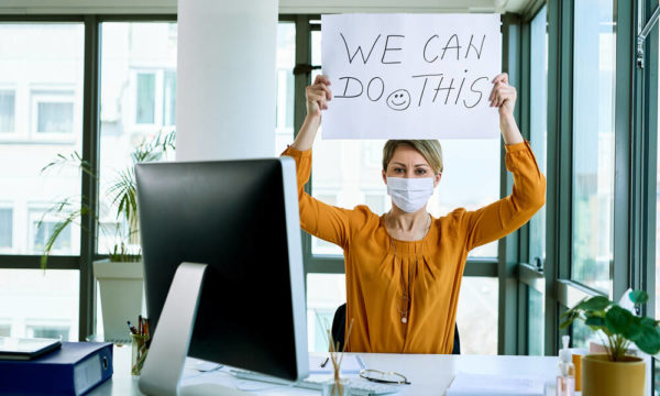 An office working wearing a mask holing up a sign that says 